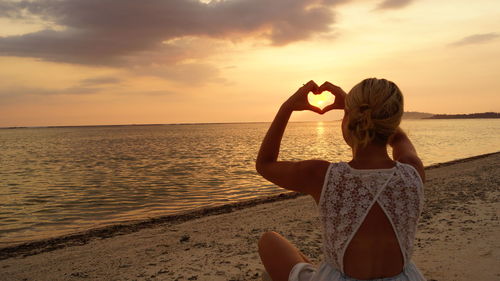 Woman making heart shape at beach during sunset