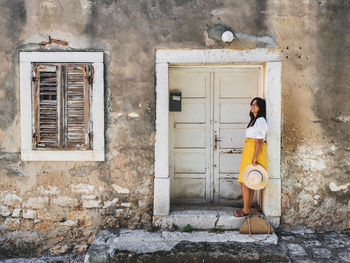 Young woman in summer outfit standing in front of old white wooden door of an old house.