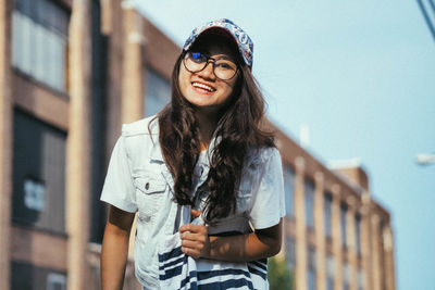 Portrait of smiling young woman wearing eyeglasses standing against building