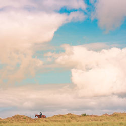 Mid distance of man horseback riding on grassy field against cloudy sky