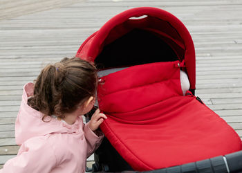 Cute girl observing her newborn brother in his covered stroller