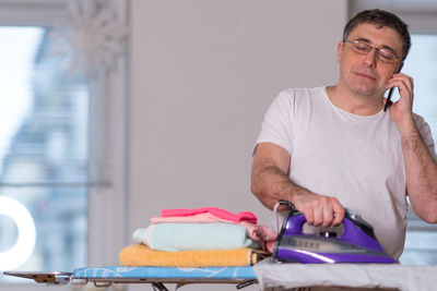 Man talking on phone while ironing cloth at home