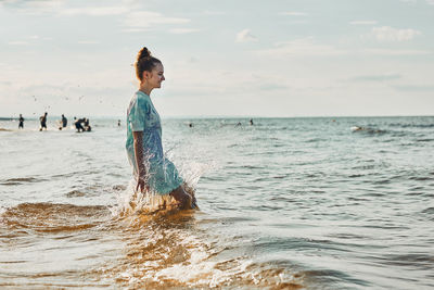 Girl enjoying sea jumping over waves spending a free time over sea on a beach at sunset