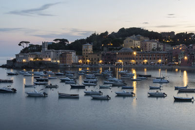 Sailboats moored in city by sea against sky at dusk