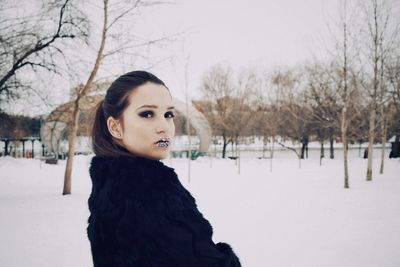 Portrait of woman standing on snowy field against bare trees