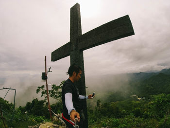 Full length of man holding cross against sky
