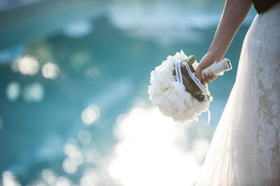 Midsection of bride wearing wedding dress while holding bouquet by swimming pool