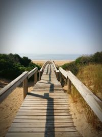 Wooden footbridge leading towards sea against clear sky