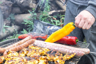 A man's hand puts a yellow pepper on a grill grate.