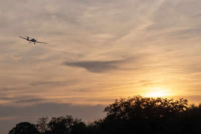 Low angle view of silhouette airplane flying against sky during sunset