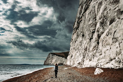 Man standing on rock by sea against sky