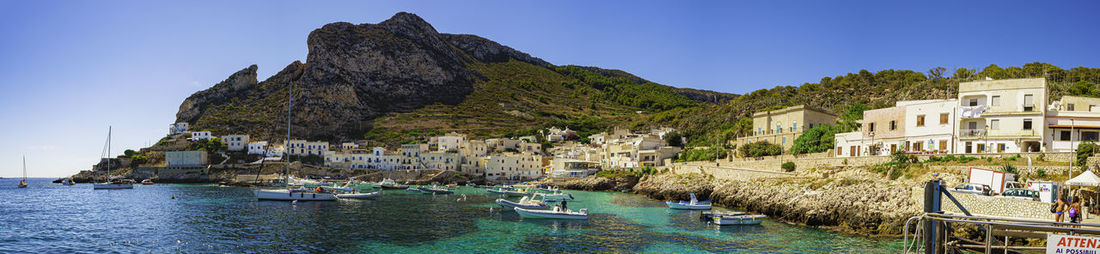 Sailboats moored on sea by buildings against clear sky