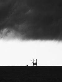 Silhouette of crane by sea against sky