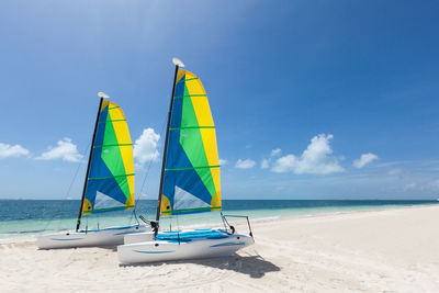 Sailboats on beach against cloudy sky