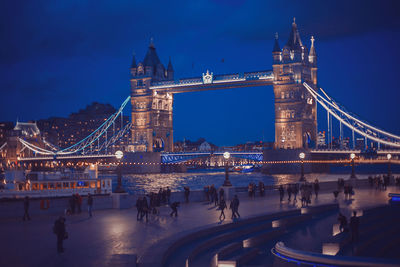 Low angle view of illuminated tower bridge over thames river at dusk
