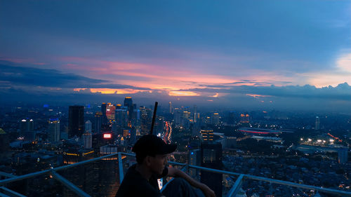 Woman looking at illuminated city buildings against sky during sunset