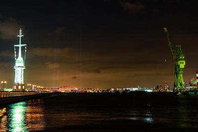 Illuminated buildings by river against sky at night