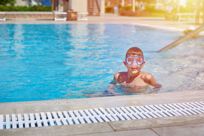 Portrait of boy in goggles standing at swimming pool