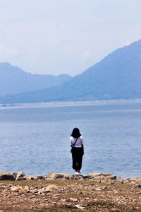 Rear view of woman standing at lakeshore against sky