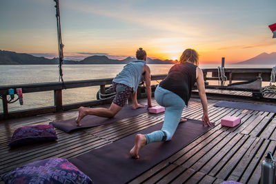 People relaxing on railing against sky during sunset