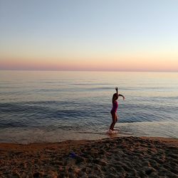 Side view of girl standing at beach against clear sky during sunset