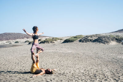 Couple doing yoga at beach against clear sky