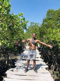 Full length portrait of happy man standing by tree against clear sky