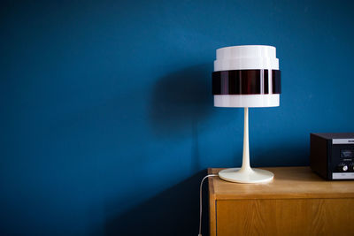 Close-up of illuminated lamp on table against wall