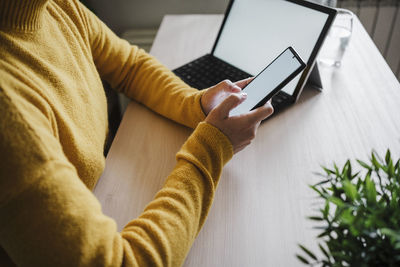 Woman using mobile phone while sitting by table at home office