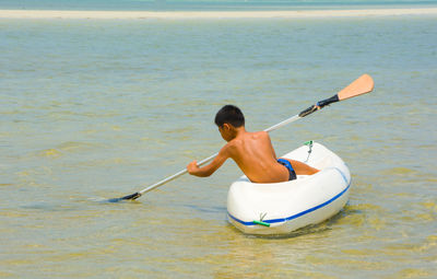 Rear view of shirtless boy kayaking in sea