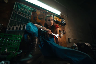 Woman holding wrench while sitting at workshop