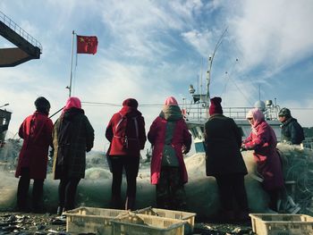Rear view of people walking on road against cloudy sky