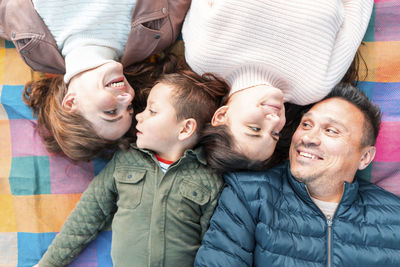 Directly above view of smiling family looking at each other while lying down on picnic blanket in park