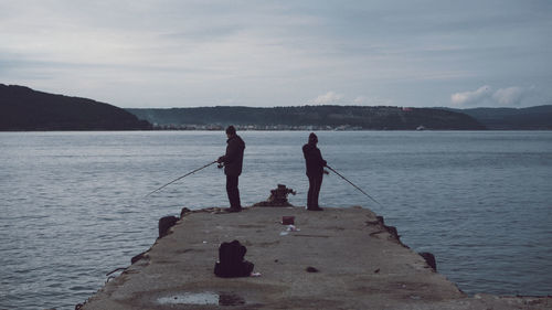 Men fishing in sea against sky