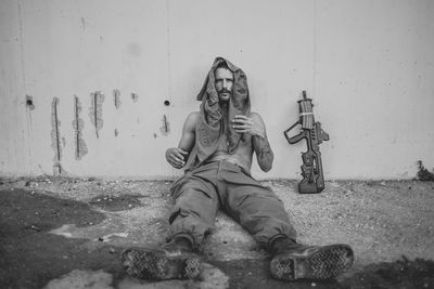 Portrait of tired soldier sitting by gun against wall