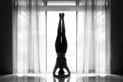 Rear view woman doing yoga on floor by window at home