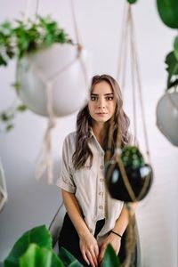 Portrait of beautiful young woman standing against potted plants