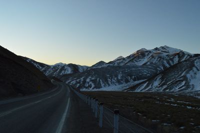 Road leading towards mountains against clear sky