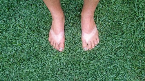 Low section of man with tan lines standing on grassy field