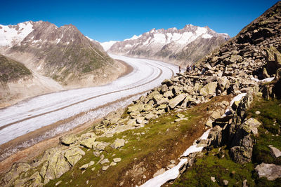 Snow covered road by mountains against clear blue sky