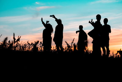 Silhouette people on land against sky during sunset