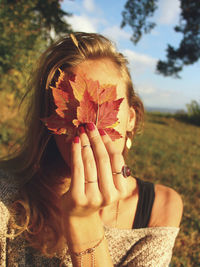 Close-up of woman holding maple leaves in front of face on field