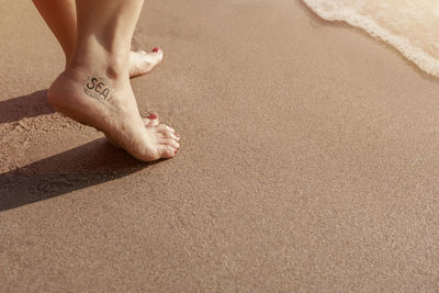 Low section of woman with tattoo walking on shore at beach