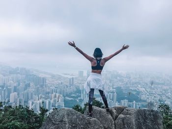 Rear view of woman with arms outstretched against buildings in city