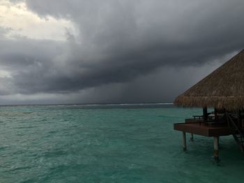 Resort hut at sea against cloudy sky