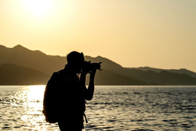 Silhouette woman standing against sea during sunset