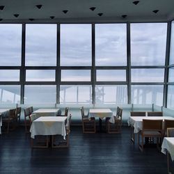 Empty chairs and tables against sky seen through glass window