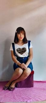 Portrait of a young woman sitting against wall