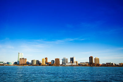 Sea by buildings in city against blue sky