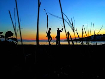 Silhouette men standing on shore against sky during sunset
